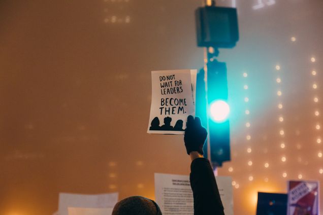 Person holding sign stating "Do not wait for leaders become them."