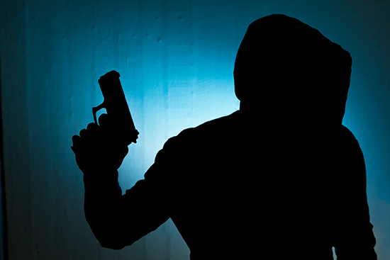 silhouette of a hooded person brandishing a gun