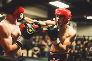 Two men wearing helmets boxing with one punching the other in a ring.