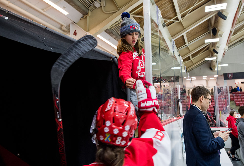 An 11 year old female fan gives a BU hockey player a fist bump before going out onto the ice.