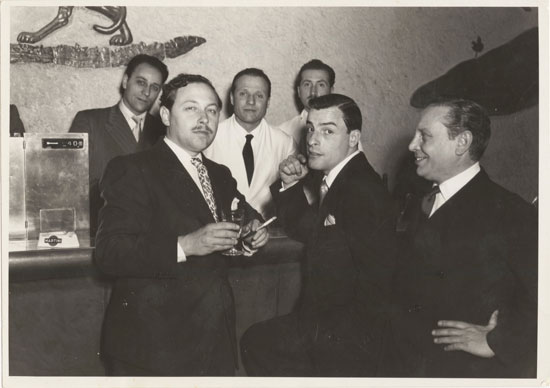 Williams and Merlo at a bar with some others, all wearing suits