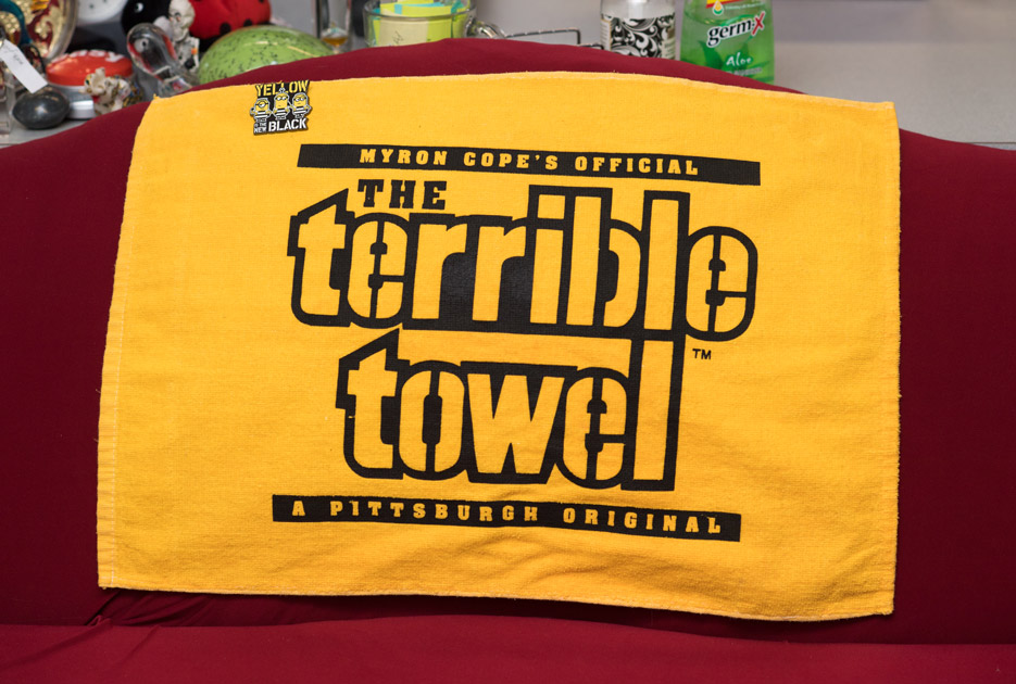 towel that says 'Myron Cope's Official The Terrible Towel TM A Pittsburgh Original', with a pin of minions in prisonwear on it that says 'Yellow Is The New Black'