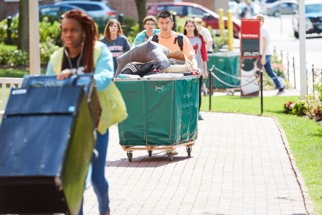 students push wheeling carts carrying their belongings on move in day