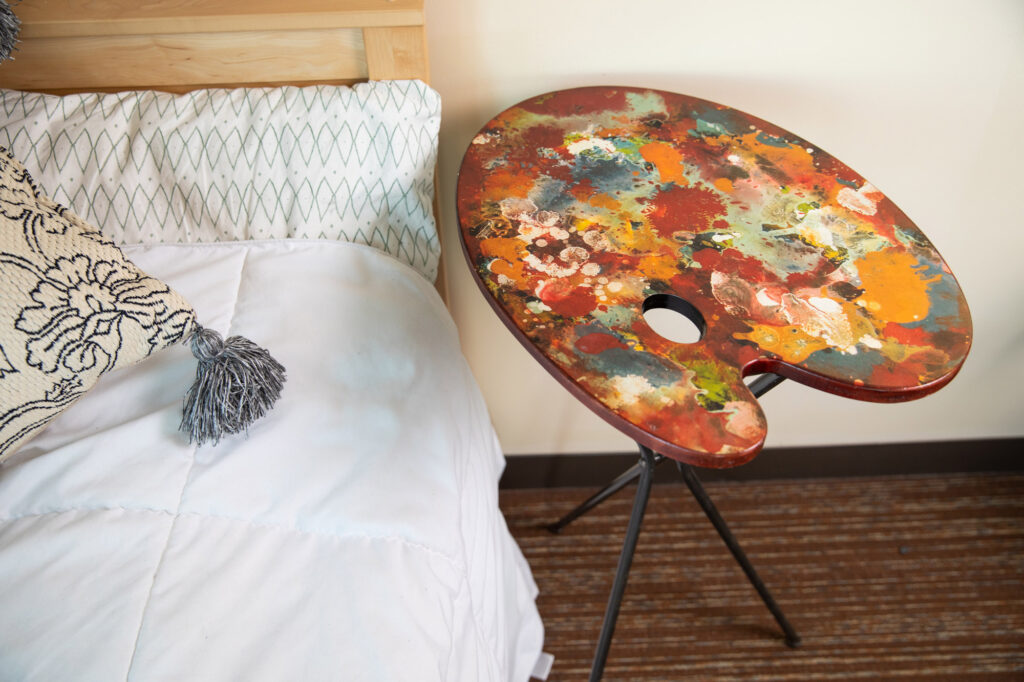 A painter's pallet serves as a side table next to a bed 