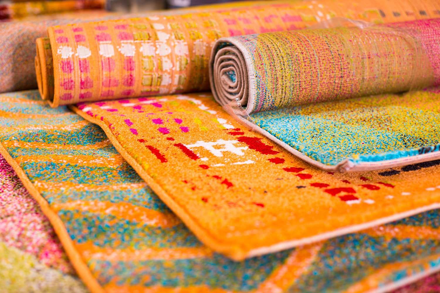 a staggered stack of colorful area rugs, partly rolled up.