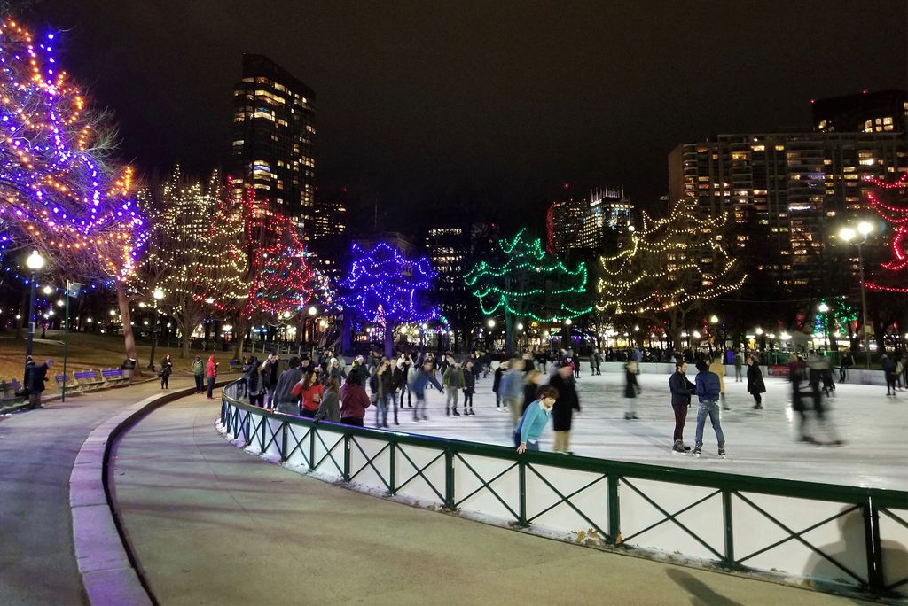 Holiday lights shine as people Ice skate on Boston Frog Pond at night.