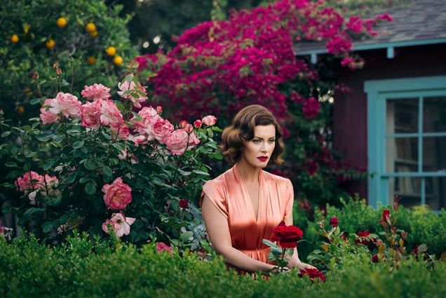 A woman poses for a photo in a garden of roses as part of Elisabeth Caren’s Double Identity series.