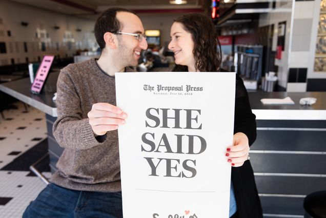 A photo of Rick Sobey (COM'12) and Felicia Gans (COM'17) holding a mock newspaper and a headline asking “Felicia, Will You Marry Me?”