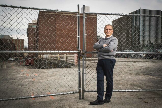 Portrait of Azer Bestavros who looks through a chain link fence towards the site of BU's new Data Sciences building.