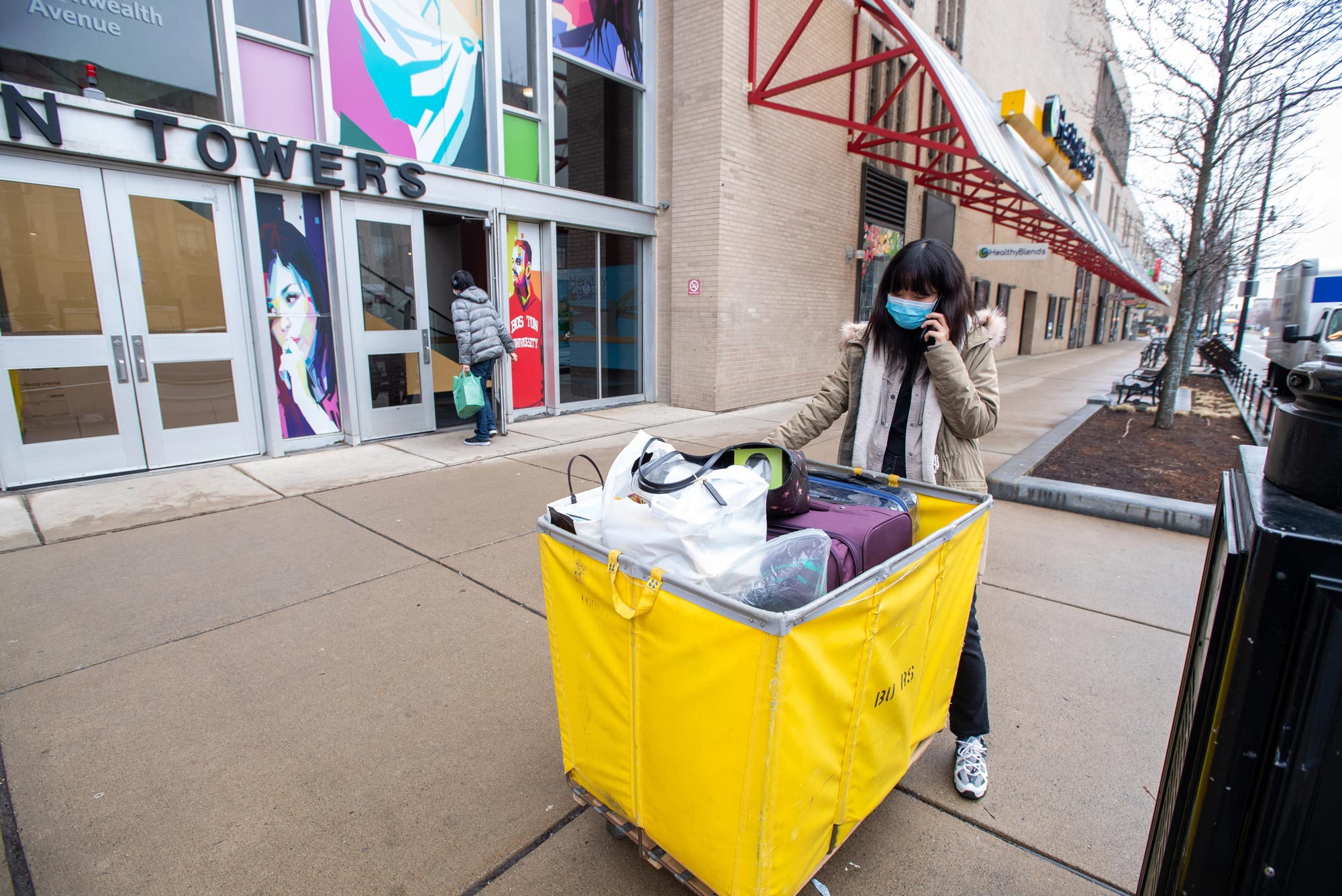 A photo of Cathy Cao (CGS’22), wearing a mask, waits for her ride to her new off campus housing March 17, 2020.