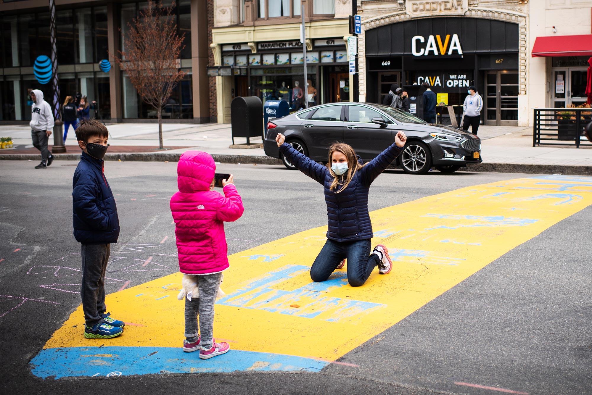 Lisa Wyman’s daughter, Alex, 5 takes a photo of her posing on the Boston Marathon finish line as her son, Anderson looks on on April 20, 2020. Photo by Jackie Ricciardi