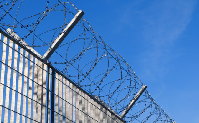 A photo of a fence topped with barbed wire.