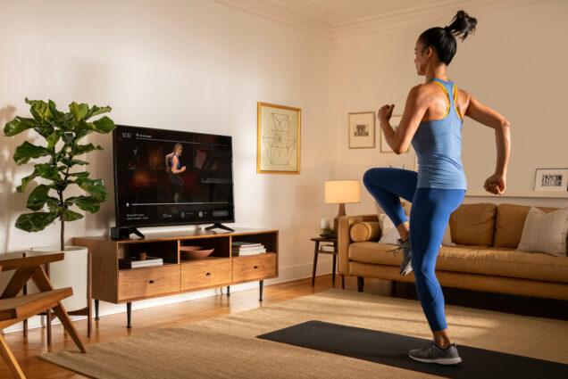 Image of a woman exercising in her home, following an instructor on the TV.