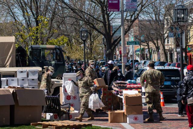 Images of local volunteers along with the National Guard distributing food to locals at Winnisimmet Park in downtown Chelsea April 23, 2020. Many boxes say "Salvation Army" on the side, and a line of people with masks is seen in the background.