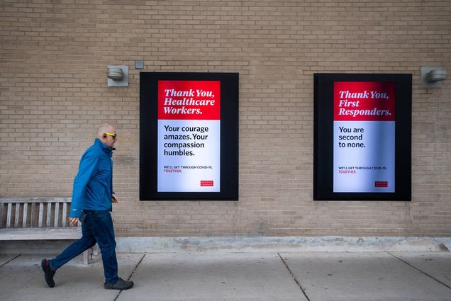 Image of two digital sign boards outside of Warren Towers as a person in a blue jacket and glasses walks briskly by. The left sign reads “Thank you healthcare workers. Your courage amazes. Your compassion humbles.” The right sign says “Thank your first responders. You are second to none.”