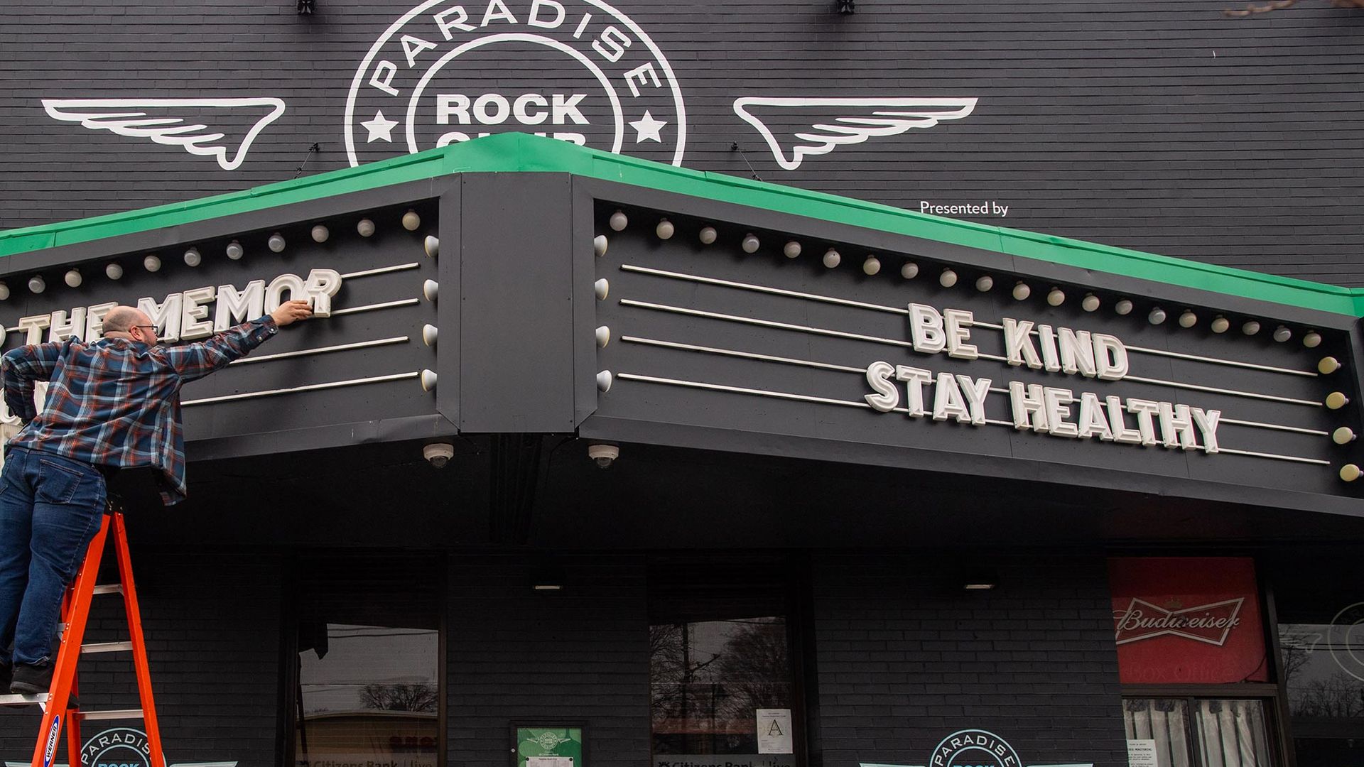 Image of Will Powell, assistant production manager at The Paradise Lounge on Commonwealth Ave, balancing on a bright orange ladder as he updates the club’s marquee to honor Tom Brady with “Thanks for the memories, Tom GOAT” and remind passers by to “Be Kind. Stay Healthy” on March 17, 2020.