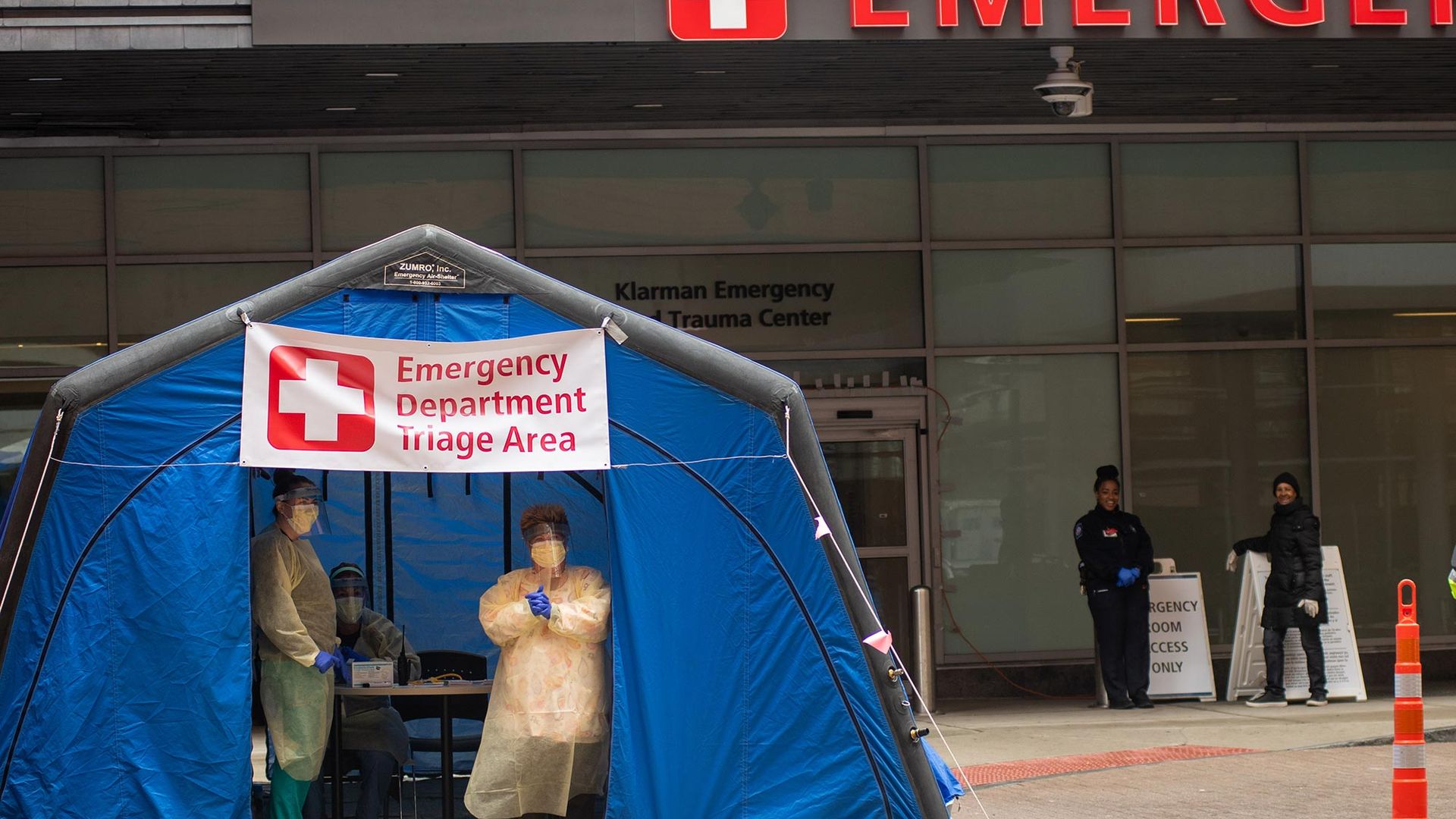 Image of Marisa McIntyre, RN, left, and Maureen Shanahan-Frappier, RN, waiting for patients outside Boston Medical Center March 20, 2020 in a blue tent with a sign that says "Emergency Department Triage Area."