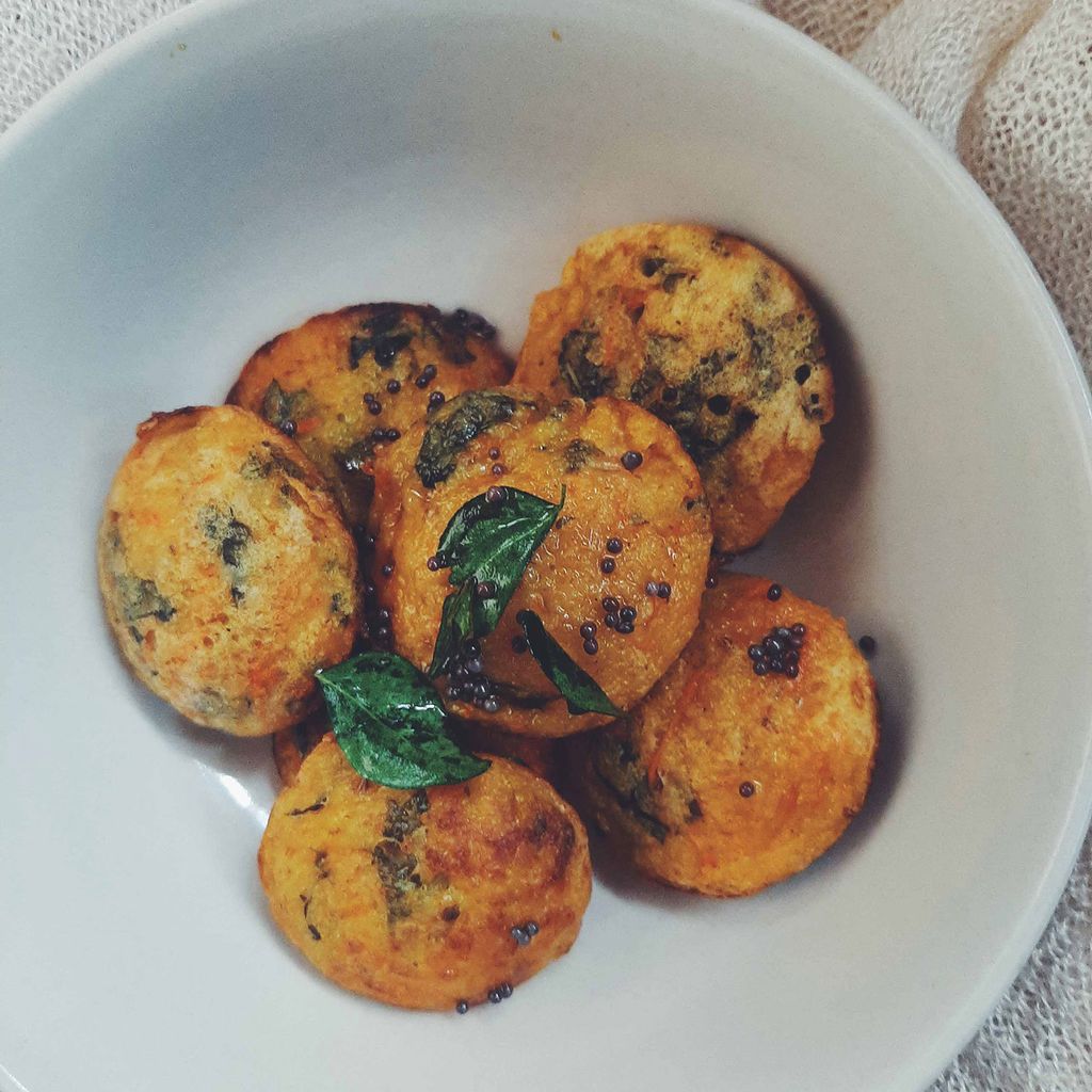 Photo spinach and carrot paniyaram, a South Indian breakfast dish made by steaming batter in a mold. 6 paniyaram sit in a white bowl.