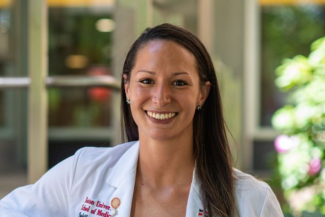 Portrait of Isa Gell-Levey (MED’22) in a white medical coat and a red dress.