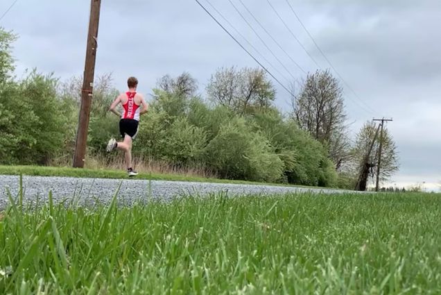 Photo of long-distance runner, Rylan Pettit (ENG’23), running down a street. Grass is seen in the foreground, Pettit wears his BU jersey. Pettit made a video discussing his improvised training regimen when the pandemic sent him home to Virginia for remote learning.