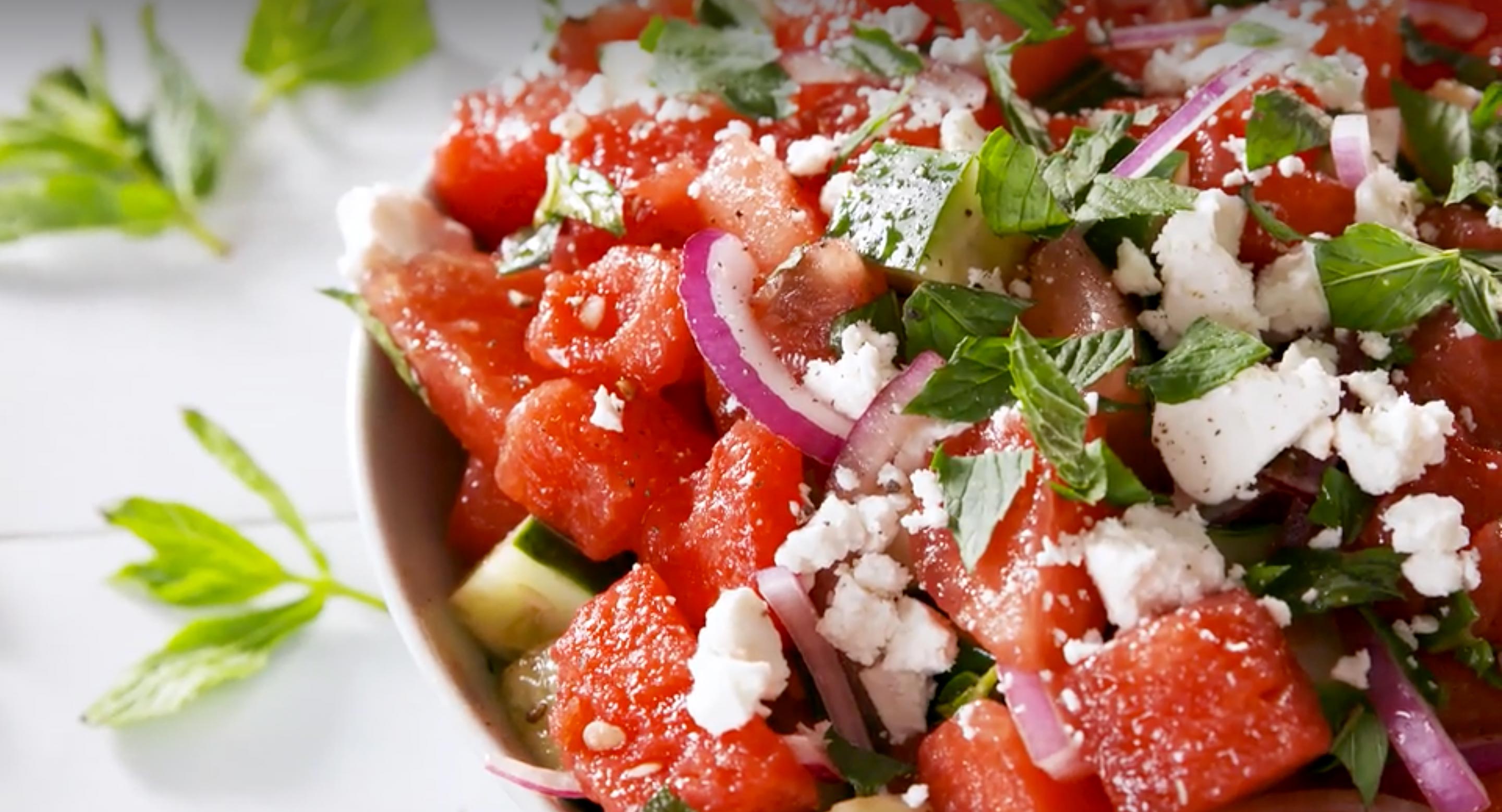 Closeup shot of a bowl of watermelon and cucumber salad with feta and mint.