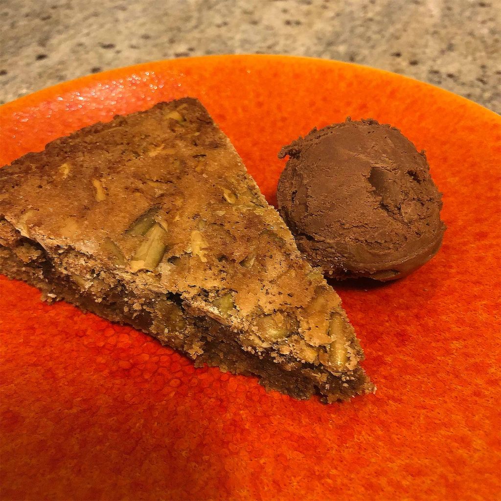 Mexican chocolate cake with pepitas and ancho chile infused chocolate gelato sits on a bright orange plate.