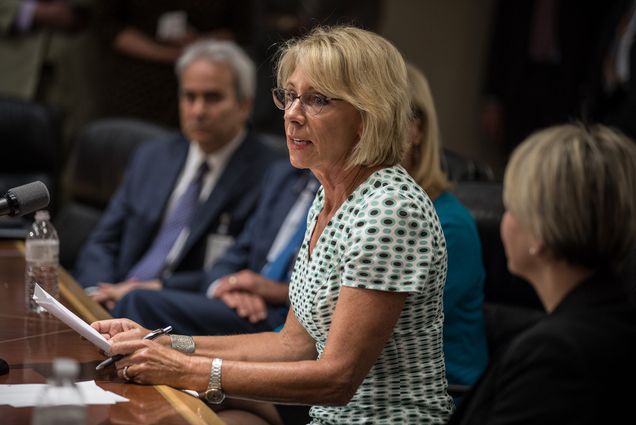 Photo of Secretary of Education, Betsy DeVos, holding a press conference at the Department of Education July 13, 2017, after a day of meetings weighing whether to keep or reject Obama-era guidance that laid out how schools must meet their obligations under Title IX, a federal law that prohibits sex discrimination at federally funded institutions. Devos wears a spotted shirt and glasses, holds papers, and speaks near a mic.