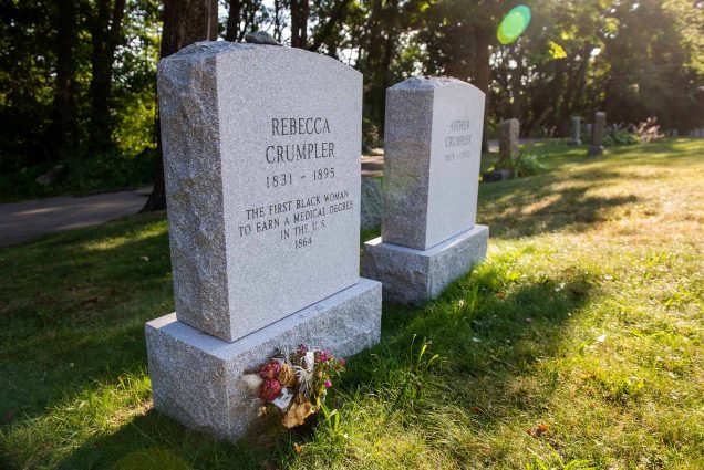 Photo of the headstones of Rebecca Lee Crumpler (MED'1864), reading "the first Black woman to earn a medical degree in the US." and her husband Arthuer Crumpler. The headstones are at the Fairview Cemetery in Hyde Park. Bright green grass grows around the headstones.