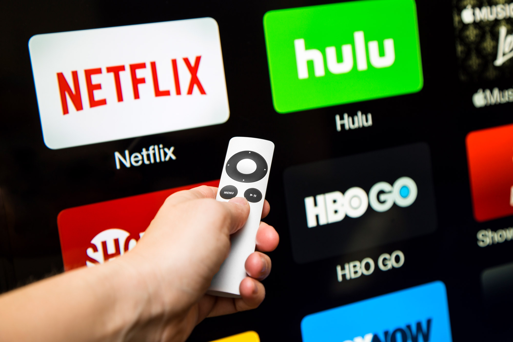 A photo of a person pointing a remote at a television screen with streaming services displayed