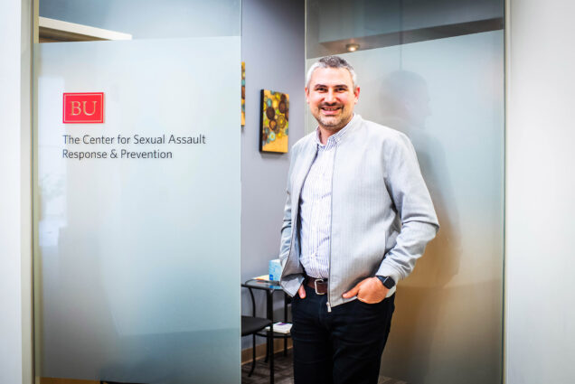 A photo of Nathan Brewer standing in front of a sign that reads "Center For BU Sexual Assault Response & Prevention"