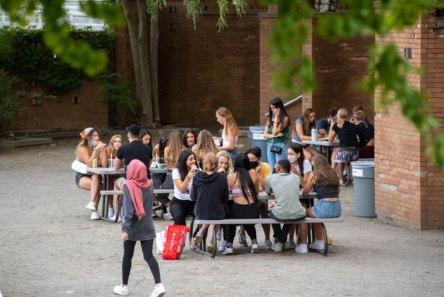 Photo of large groups of mostly unmasked students eating and hanging out at picnic tables on West Campus on August 28.