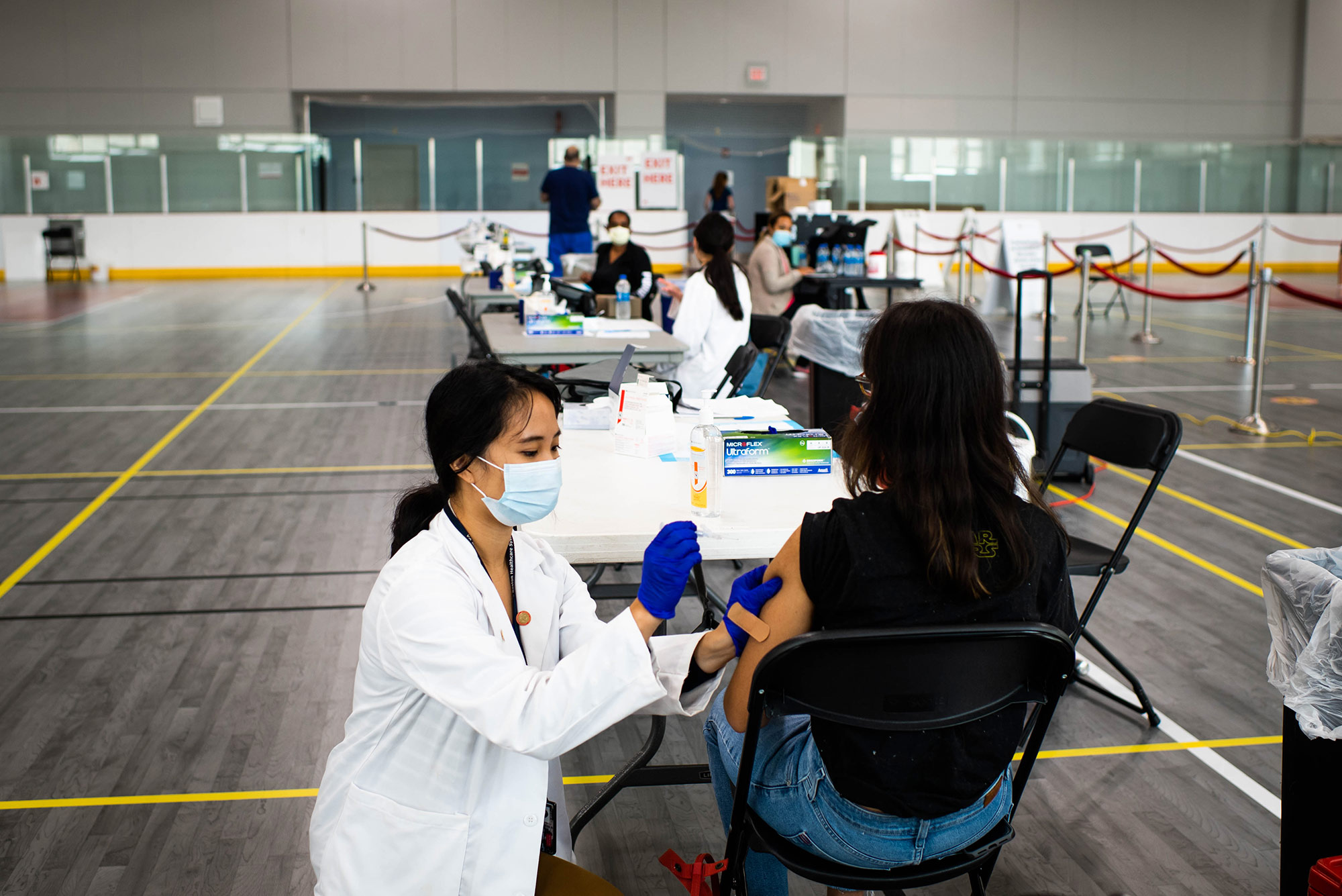 Photo of BU Medical student, Molly Jia Yong Zhao giving a flu shot to a patient during a clinic on September 29, 2020. Behind them are several other tables where flu shots are being administered.