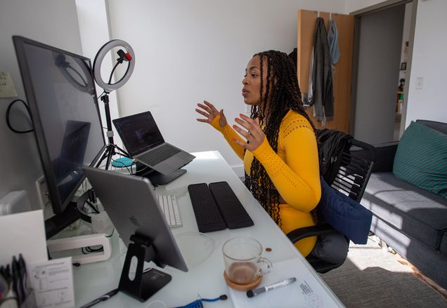 Photo of Saida Grundy, a CAS assistant professor of sociology, teaching her Race, Class and Gender course from the “cockpit” in her home September 29. She wears a bright orange outfit and speaks to her students on screen.