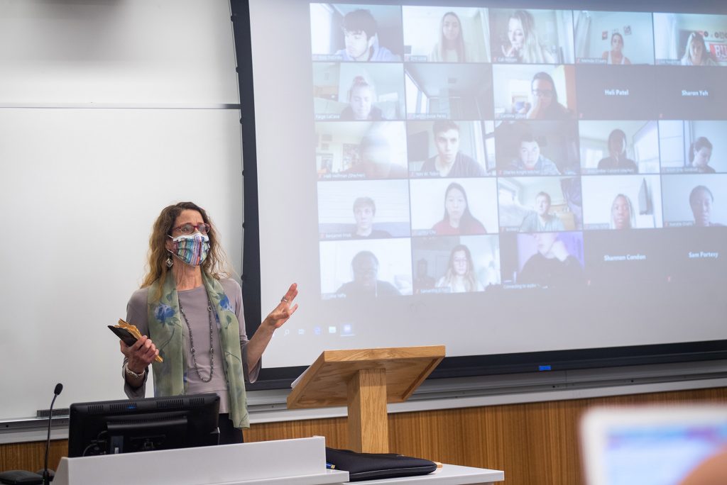 Susan Mizruchi, a CAS professor of English and director of BU’s Center for the Humanities,  at the front of her class teaching. A projector behind her shows the faces of students in the class.