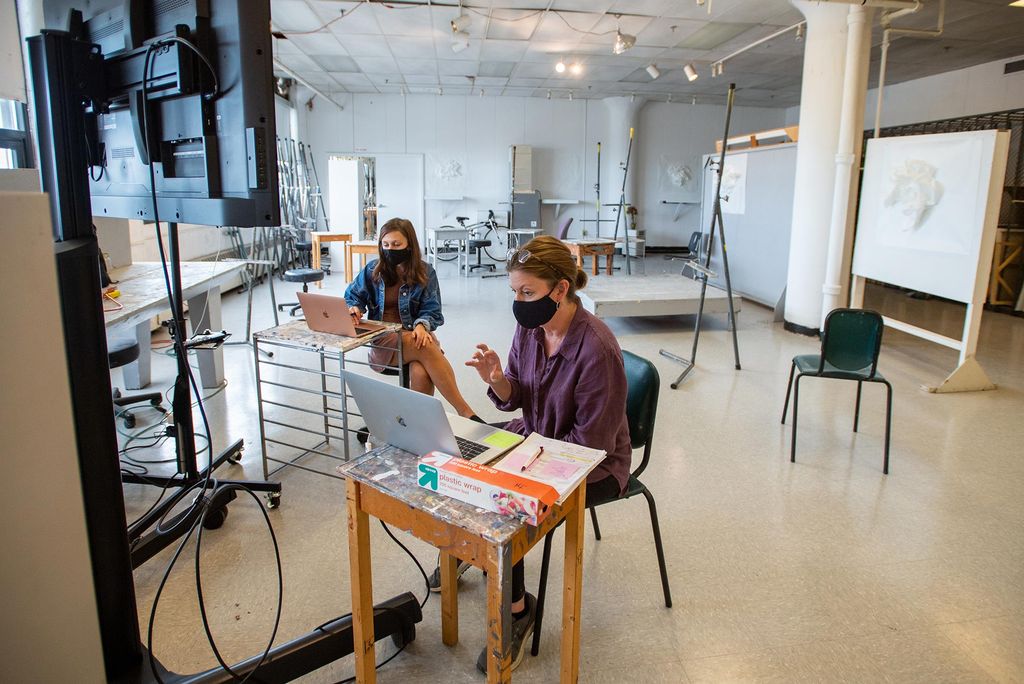 Photo of Jill Grimes (front, center) with her TA Kaitlyn Malinowski (CFA’21) in Grimes’ Painting II course. The two sit in any empty art space on campus and look at their computers.