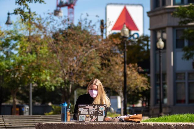 Photo of Melissa Boberg (CAS’22) studying outside in the Metcalf Science plaza on October 15, 2020. She wears a pink mask, her laptop is decorated with stickers, and the Citco sign and a red crane are seen in the background.