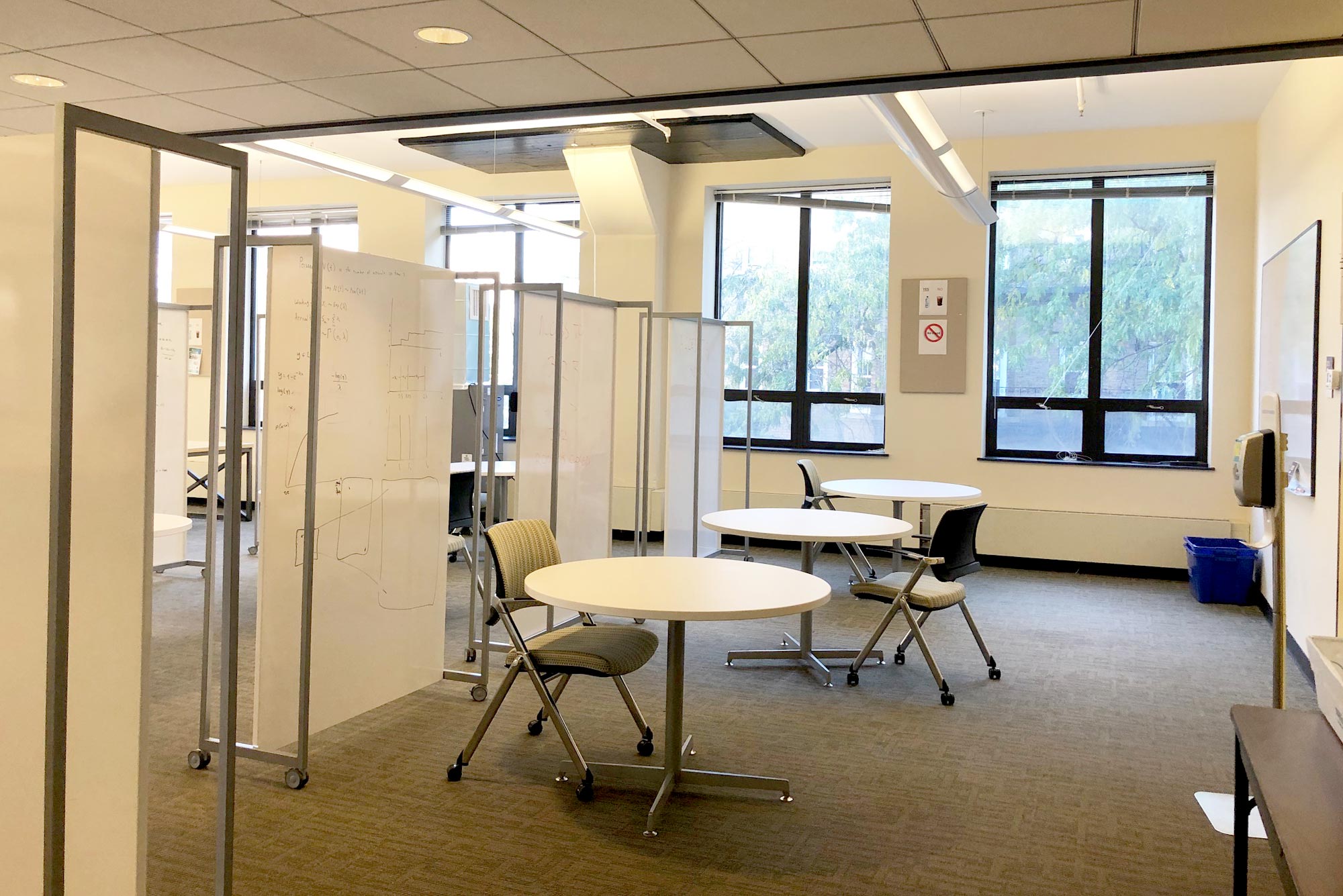 Photo of room 302 at 730 Commonwealth Ave, circular tables with single chairs are in a row divided by white boards. This space is now reservable using a new student study app.