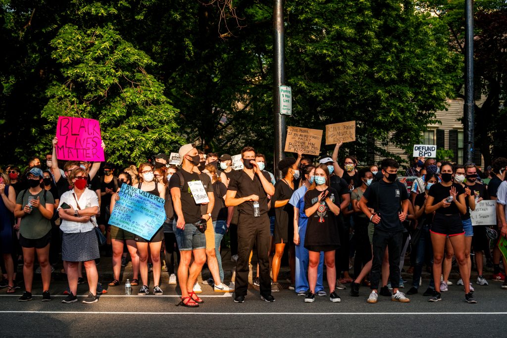 Photo of a Black lives matter protest. A group of people stand with cardboard signs wearing masks.