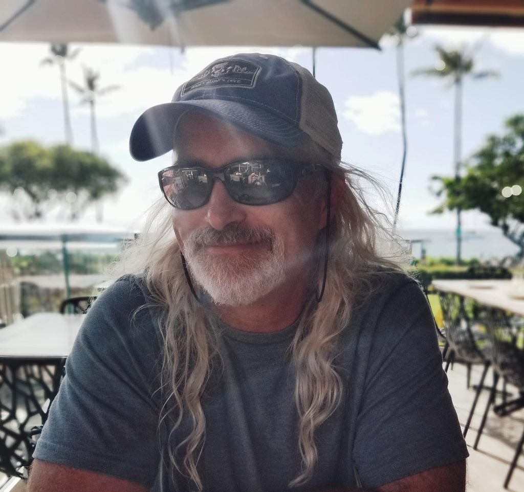 Headshot of lighting artist Dietrich Juengling in a baseball cap and sunglasses with a patio and palm trees behind him.