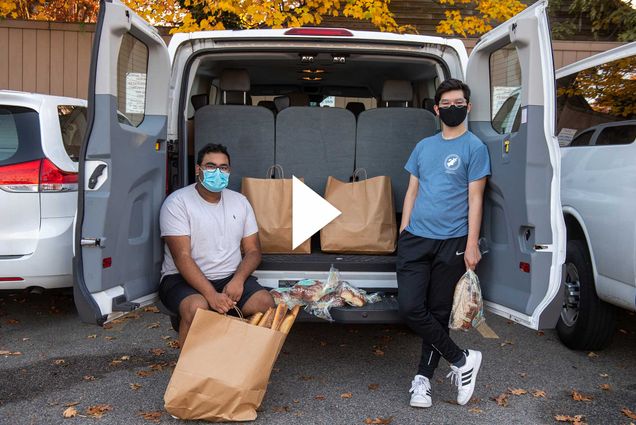 A photo of Saahil Adusumilli (SAR’22), at left, and Michael Gomez (SAR’21) from Student Food Rescue sitting in the back of a van with brown paper bags. They are both wearing masks.