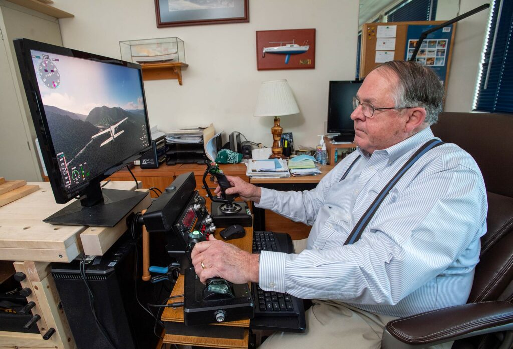 Photo of Bill Dupee, business analyst/consultant, Questrom Info Tech Services Department, sitting in front of his computer as uses different joysticks to fly a plane using a flight simulator he built with his son.