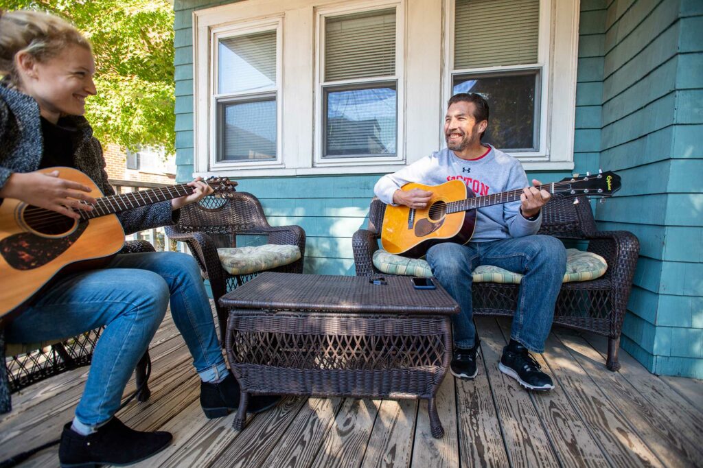 Photo of Thomas Bohrer plays some guitar with his daughter Sabrina at her home in Somerville.They sit outside on the porch of a light blue house.