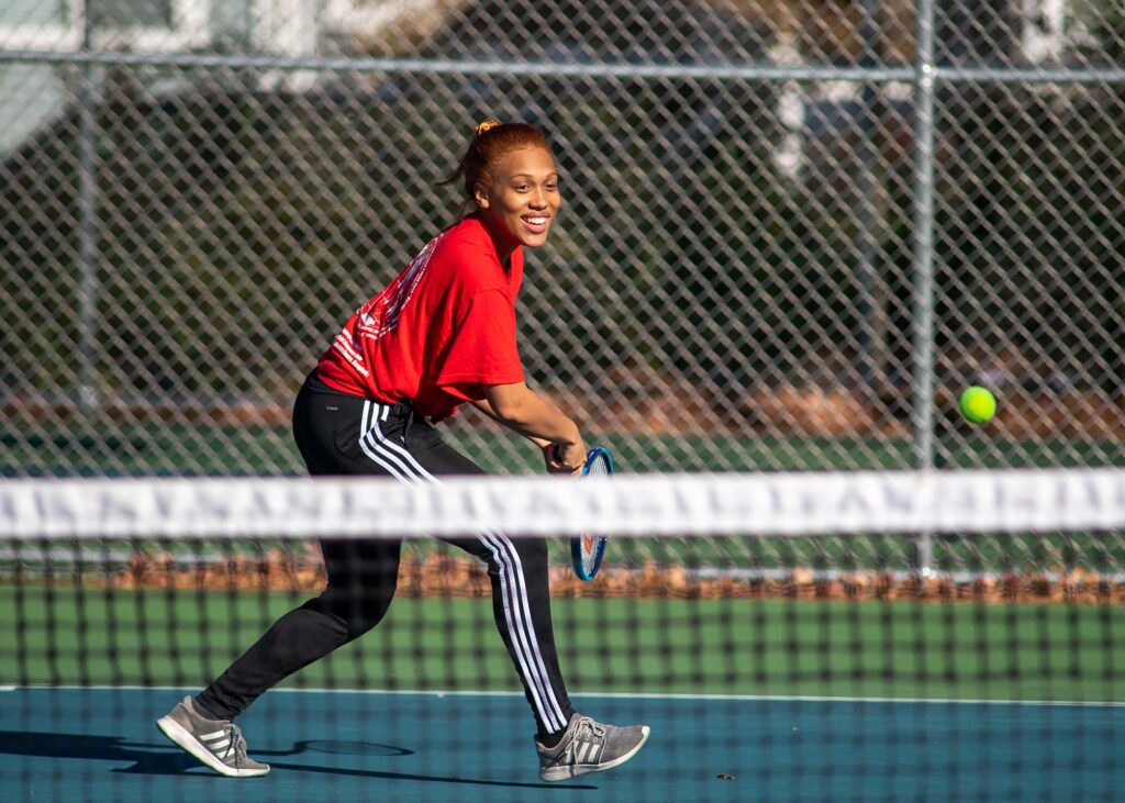 Photo of Nyah Jordan, BU Student Government vice president for internal affairs, in a red shirt and track paints, smiling, at the Harris Playground courts in Medford.