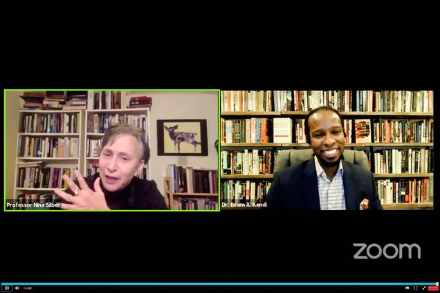 Screenshot of a the 2020 annual Howard Zinn lecture on December 7 given over zoom. Ibram X. Kendi, this year’s lecturer, smiles wide on screen, as he speaks with Nina Silber, on screen left, who also smiles and gestures with her hand. The zoom logo is seen in the bottom right corner.