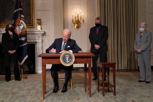 A photo of Joe Biden signing climate legislation at a desk in front of Vice President Kamala Harris and another administration officials