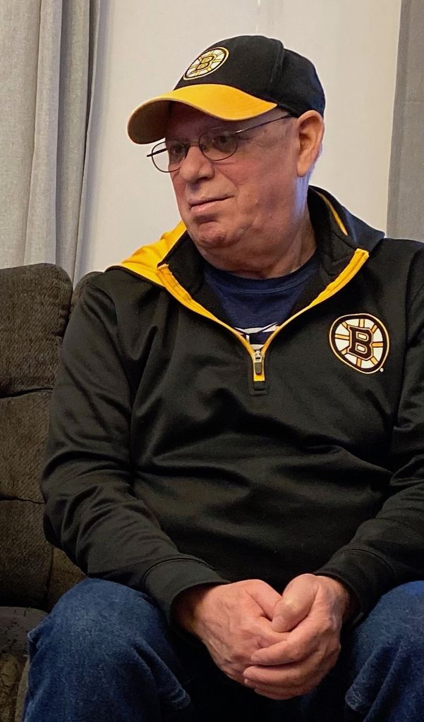 Photo of Jose Ferreira looking content while sitting on a couch in a Bruins hat and quarter zip.