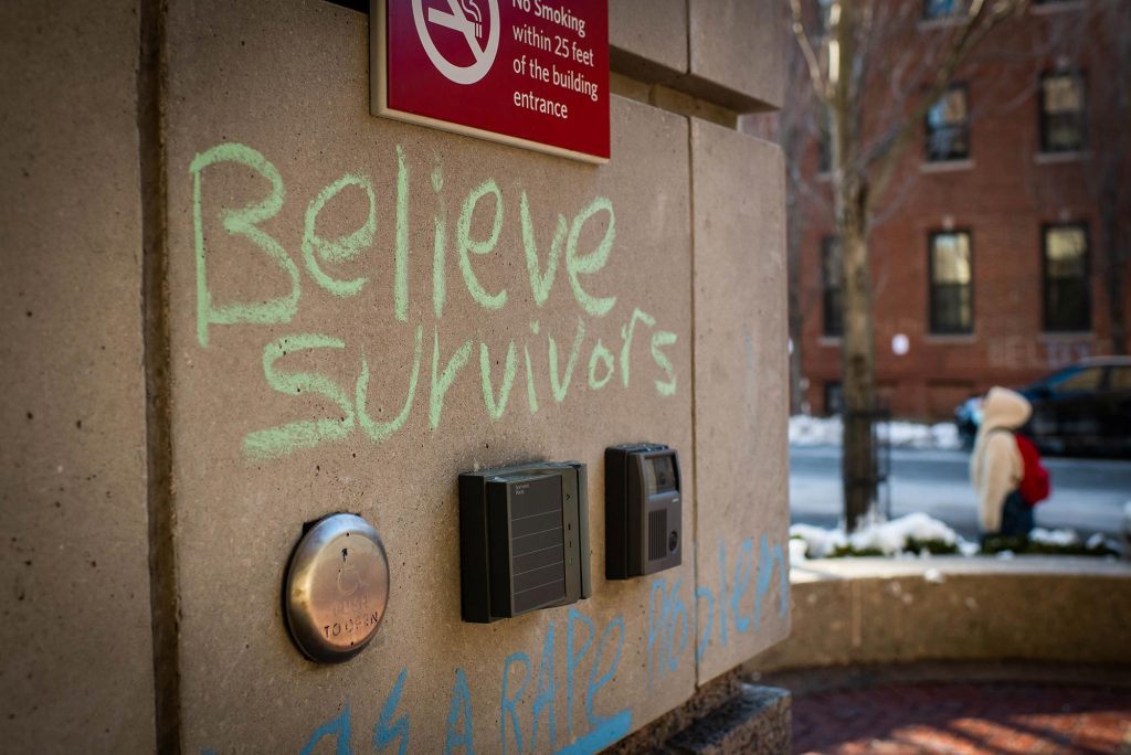 Photo of green chalk graffiti is seen on a wall outside one of the buildings on campus on February 8, 2021. The graffiti reads “believe survivors’” with lines around it.