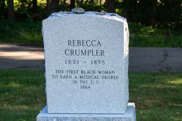 Photo of the headstones of Rebecca Lee Crumpler (MED'1864), and reads “the first Black woman to earn a medical degree in the US, 1831-1895” The headstone is located in the Fairview Cemetery in Hyde Park, and surrounded by lush, green summer grass.