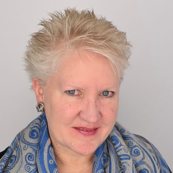 Headshot of Joanne Dennison who wears a blue, floral scarf and has short white, blondish hair.