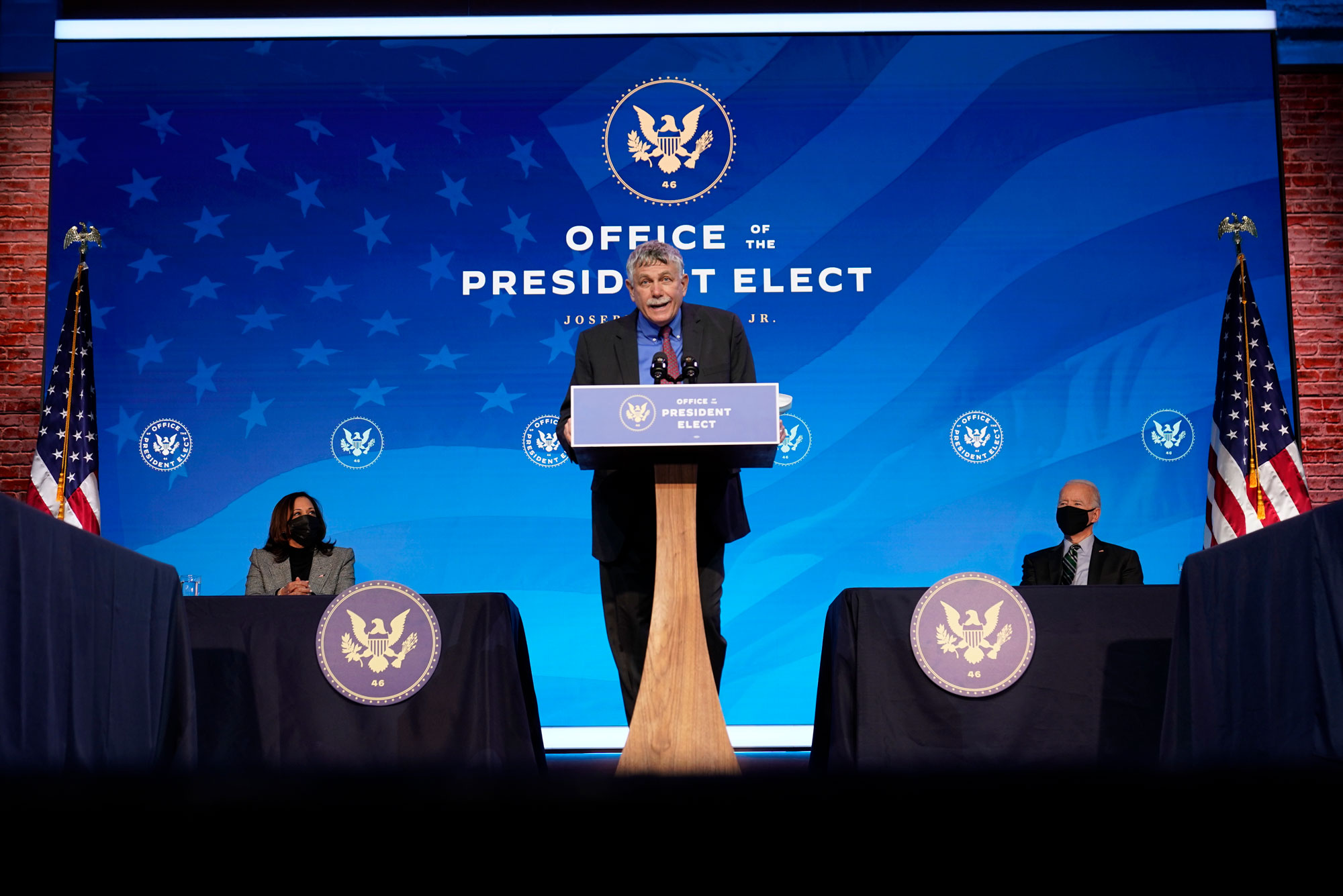 A photo of Eric Lander standing at a podium in front of a back drop that reads "Office of the President Elect"